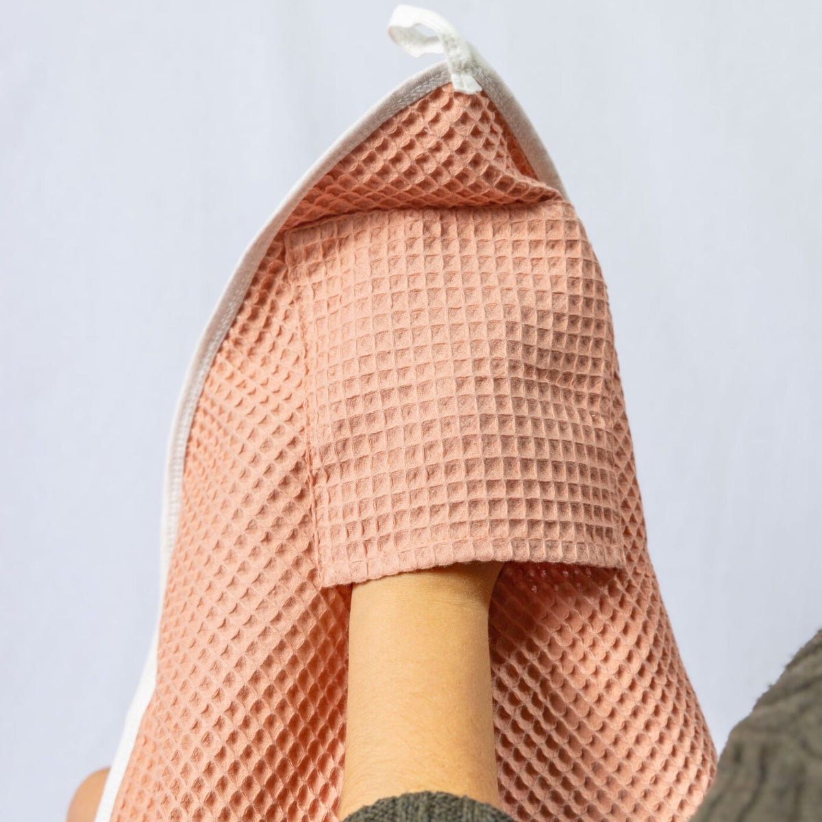 Pink textured towel hanging on a hook against a light gray background