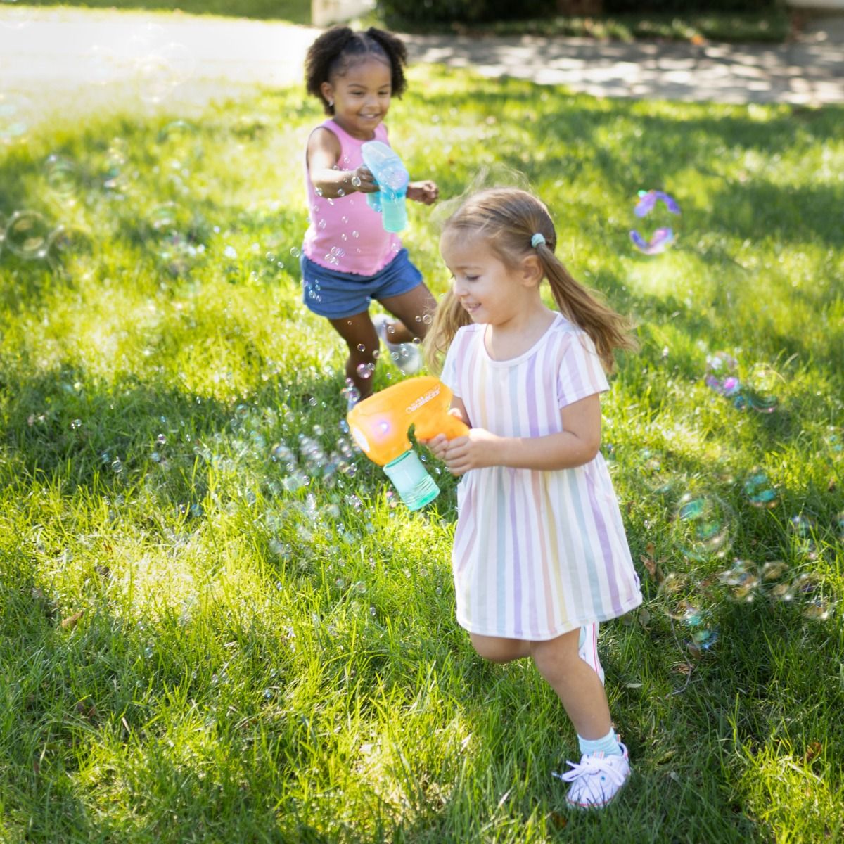 Two young girls playing with Maxx bubble guns on a grassy lawn.