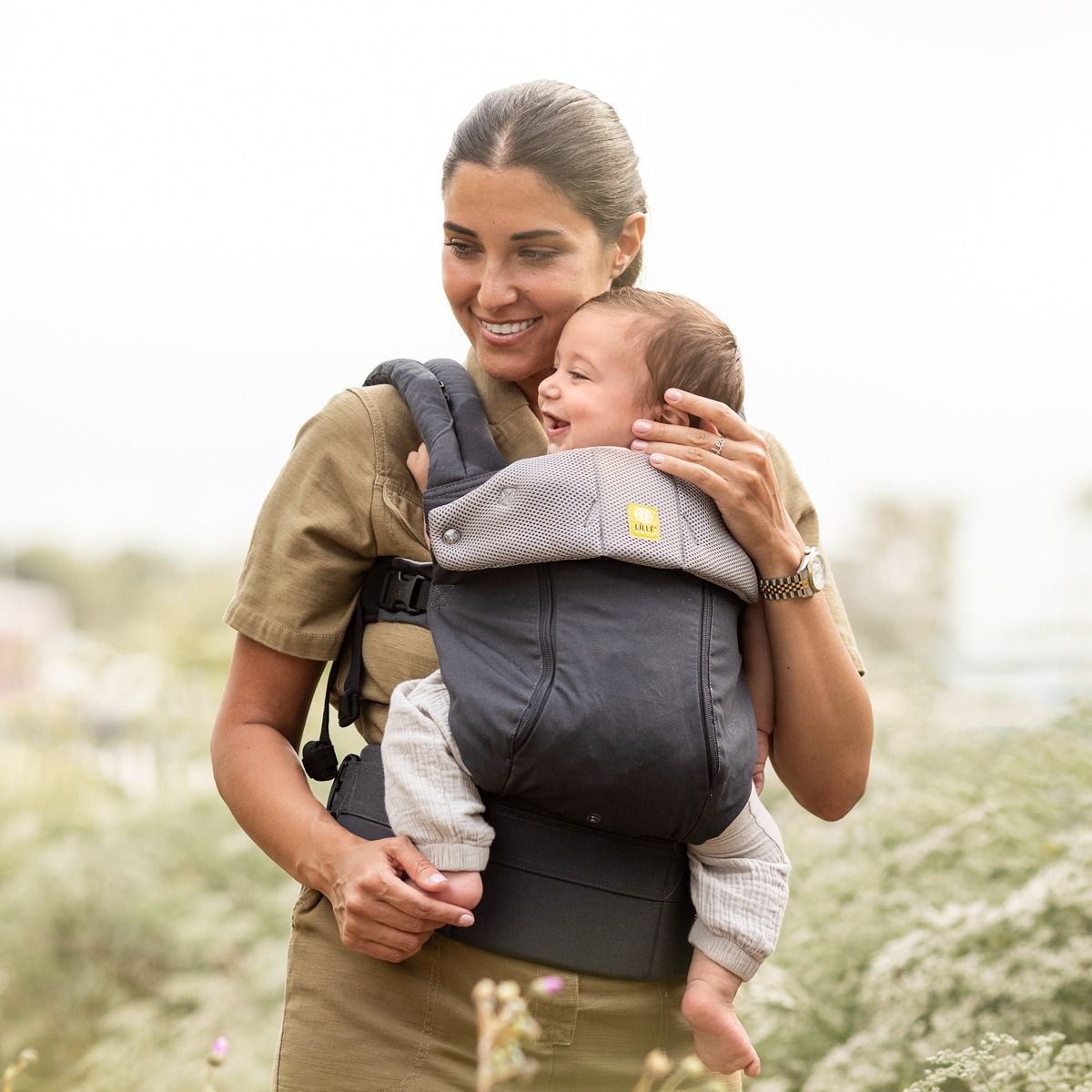 Woman holding a baby in a carrier outdoors with a blurred natural background