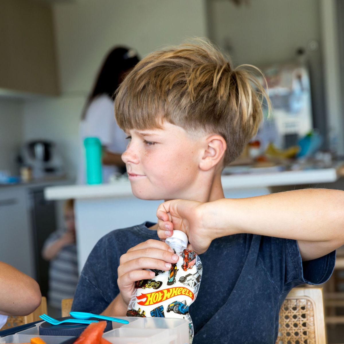 Child holding a Hot Wheels sinchie bottle in a kitchen setting