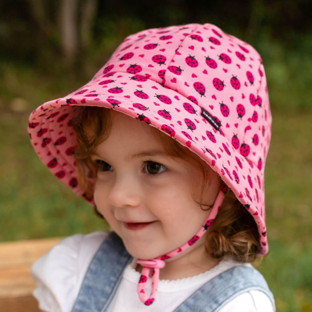 Child wearing a pink sun hat with ladybug pattern outdoors