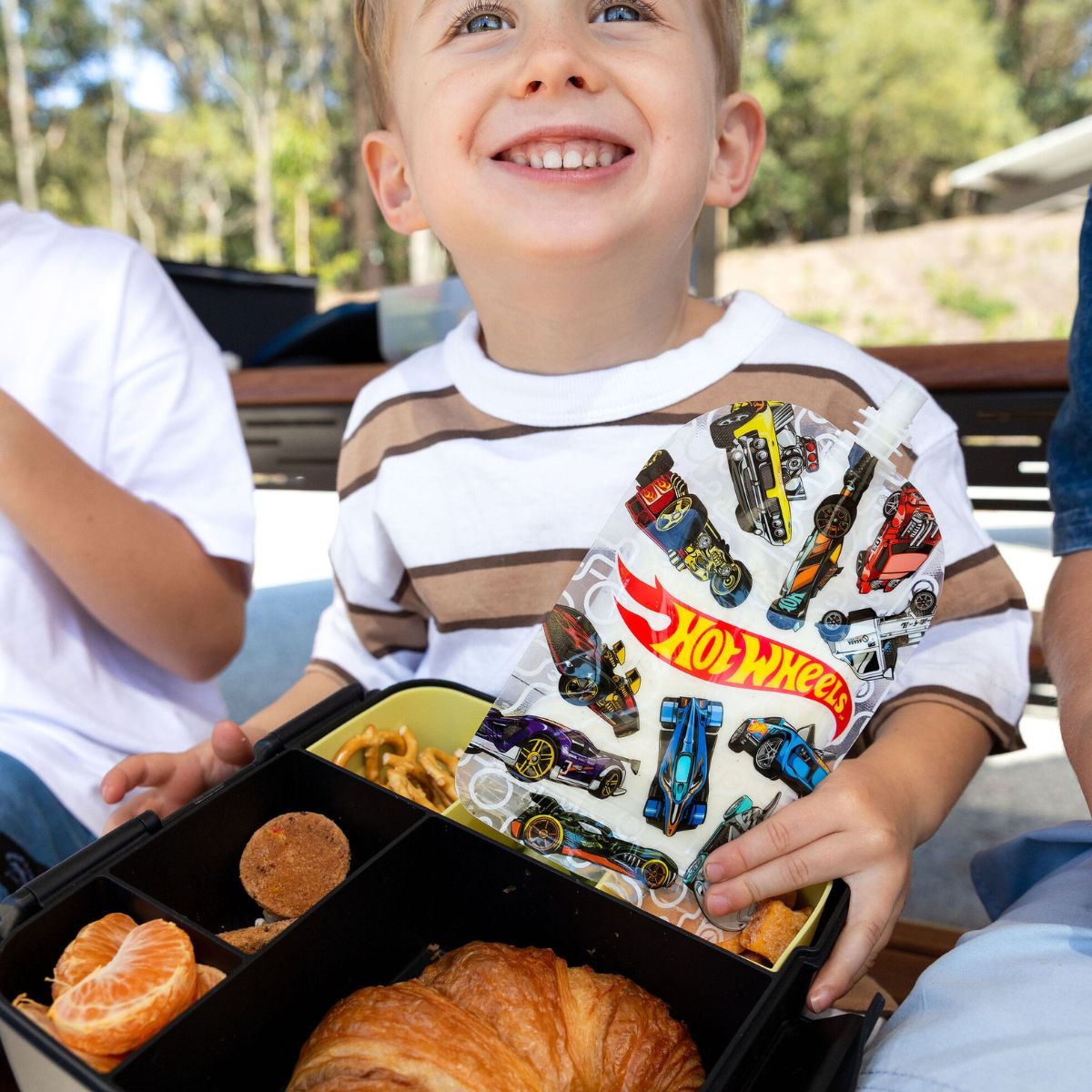 Child holding a Hot Wheels sinchie set with a box of snacks outdoors