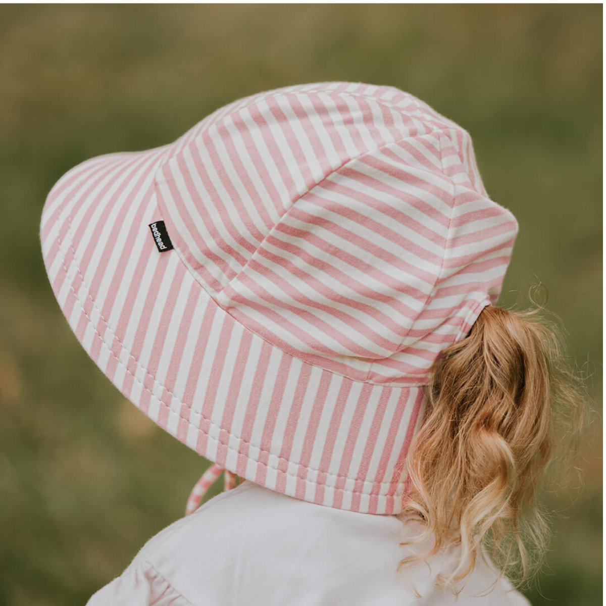 Person wearing a pink and white striped bucket hat with a blurred natural background