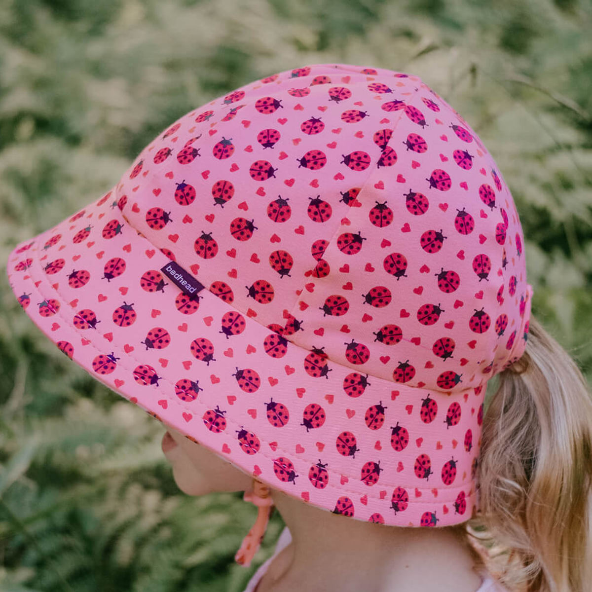 Pink sun hat with ladybug pattern worn by a child in a grassy area