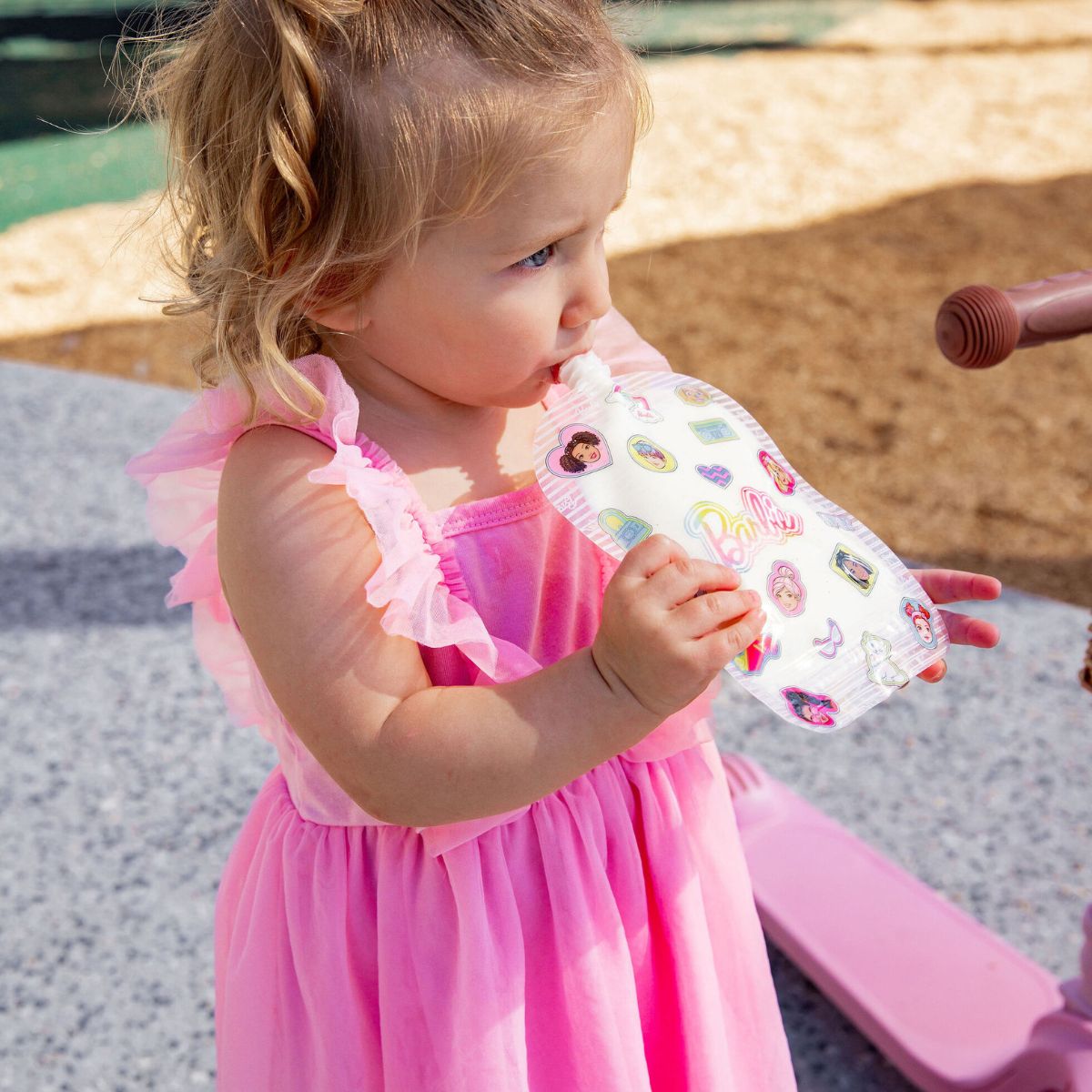 Child in a pink dress holding a colorful barbie sinchie playing outdoors