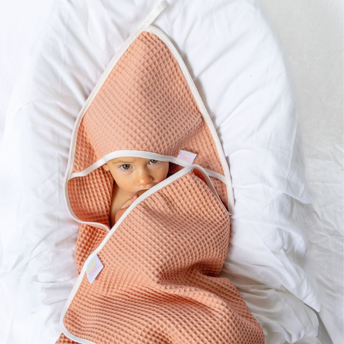 Baby wrapped in a salmon-colored hooded towel on a white surface