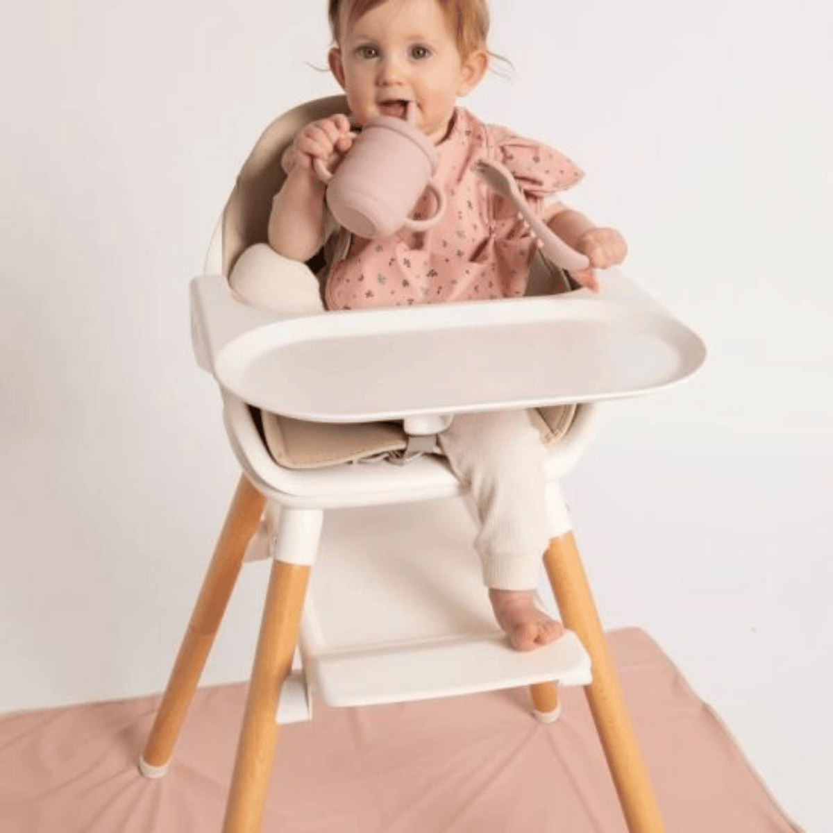 Child in a high chair holding a pink cup on a white background