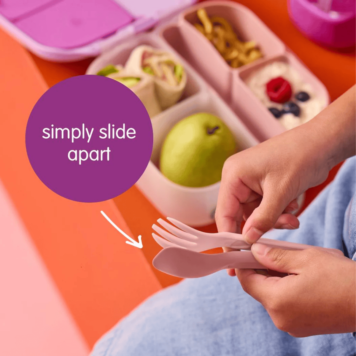 Bento box with compartments filled with food and a hand holding pink utensils on an orange surface.