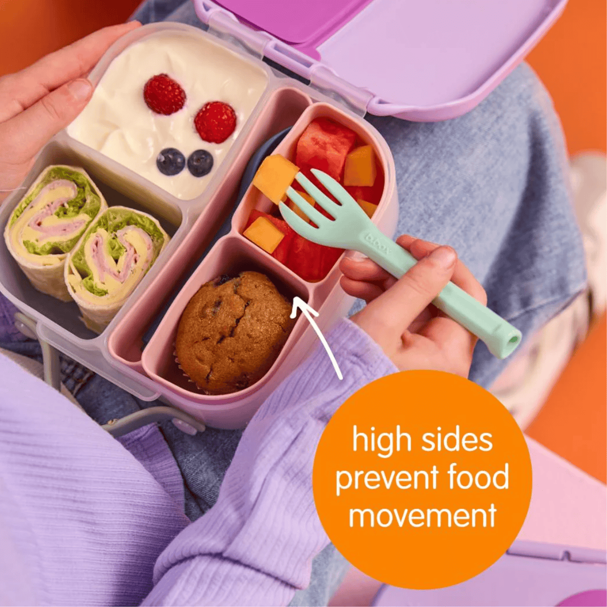 Pink bento box with compartments containing food and a fork, held by a person.