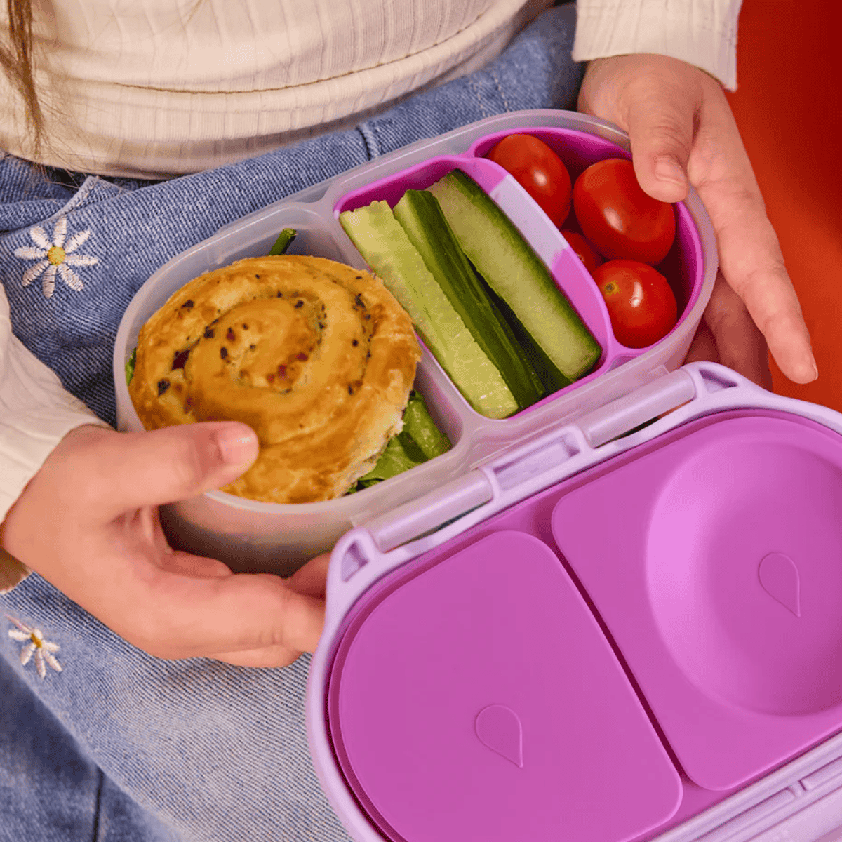 Purple bento box with a sandwich, vegetables, and tomatoes held by a person.
