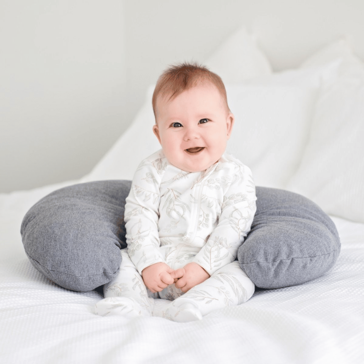 Baby sitting on a gray cushion with a white background