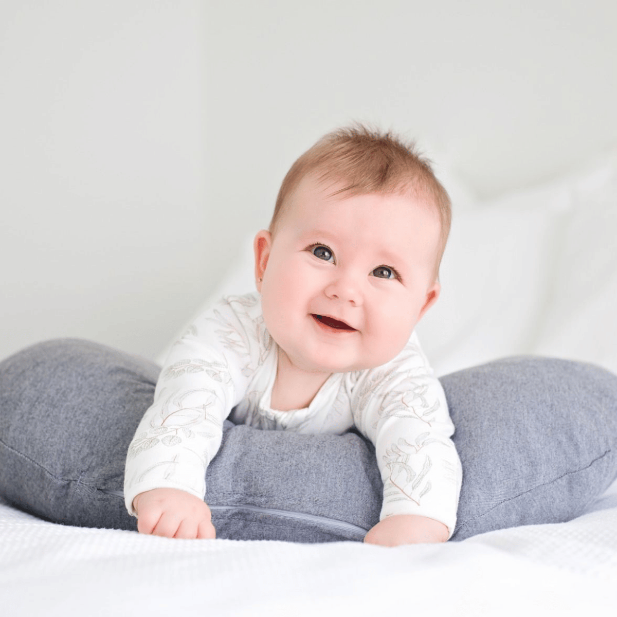 Baby lying on a gray pillow against a white background