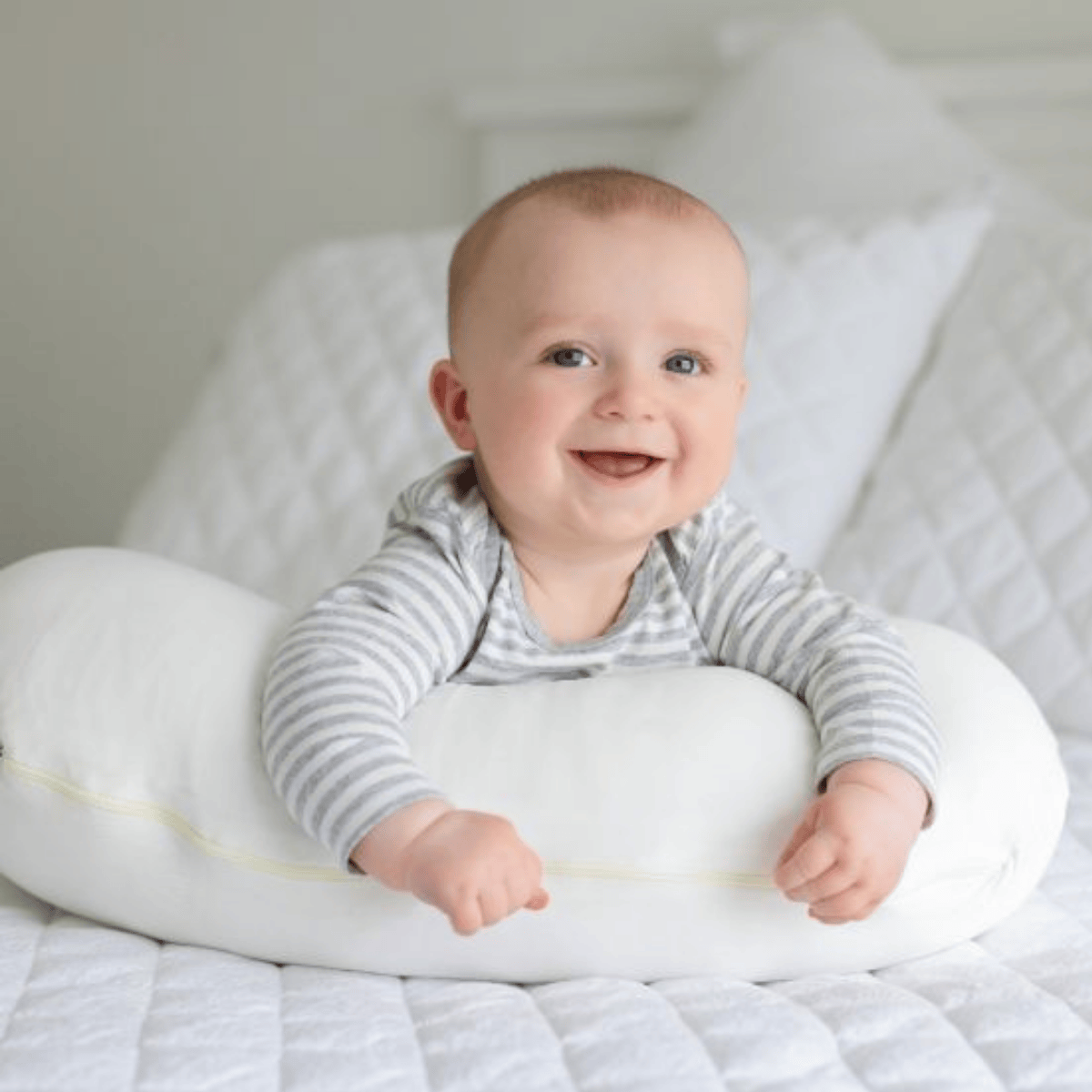 Baby lying on a white pillow with a gray and white striped shirt, smiling.