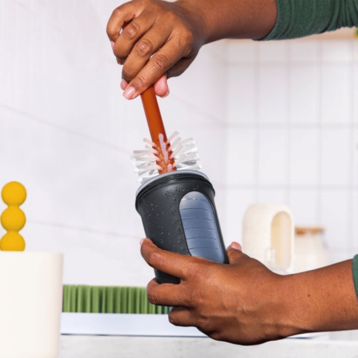 Person cleaning a black cup with a brush on a white background