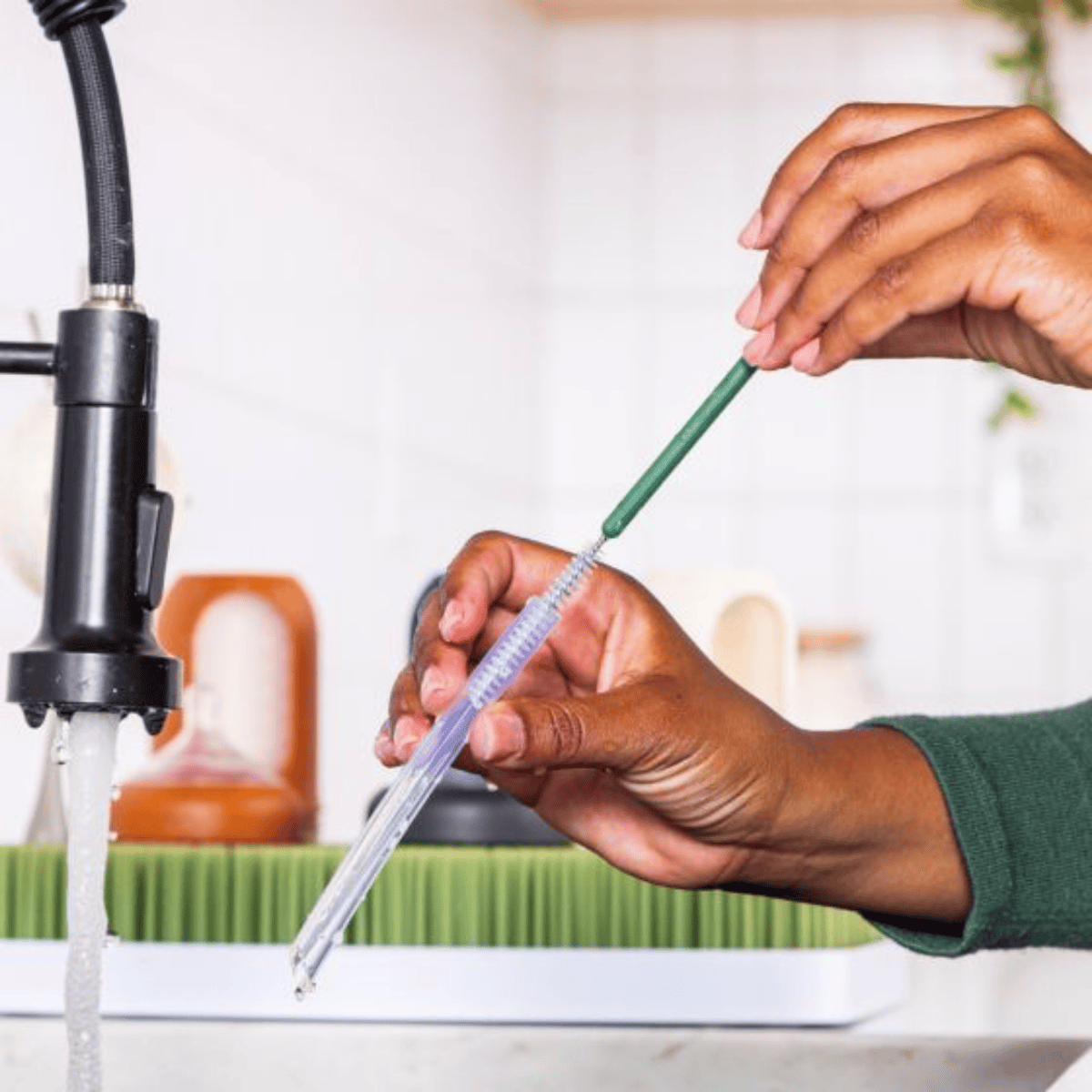 Person holding a straw under running water from a faucet