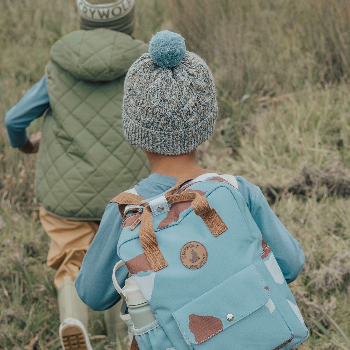 A boy showing the back of the blue speckled pom pom beanie by Crywolf.