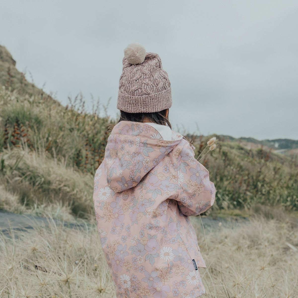 A girl outside showing the back of the Crywolf Pom Pom speckled mauve beanie.