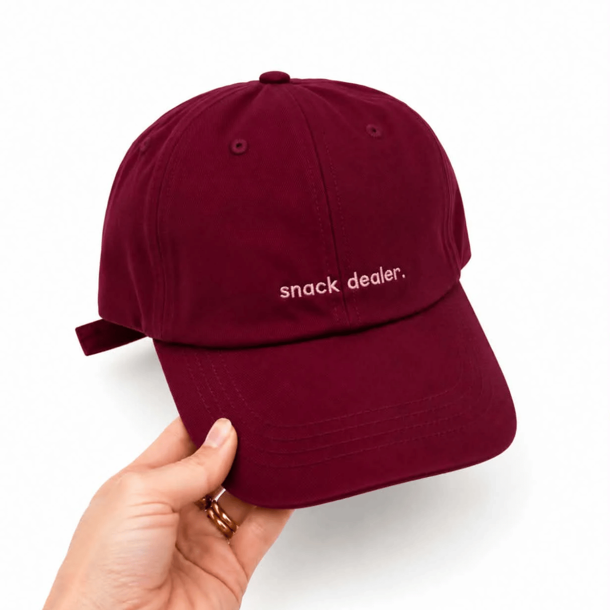 Cotton baseball cap in burgandy with the words 'snack dealer' on it. 