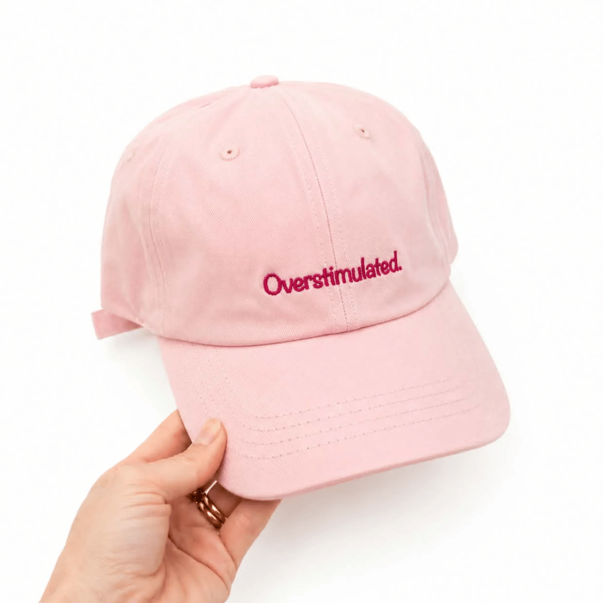 Cotton baseball cap in pink with the words 'overstimulated' on it. 