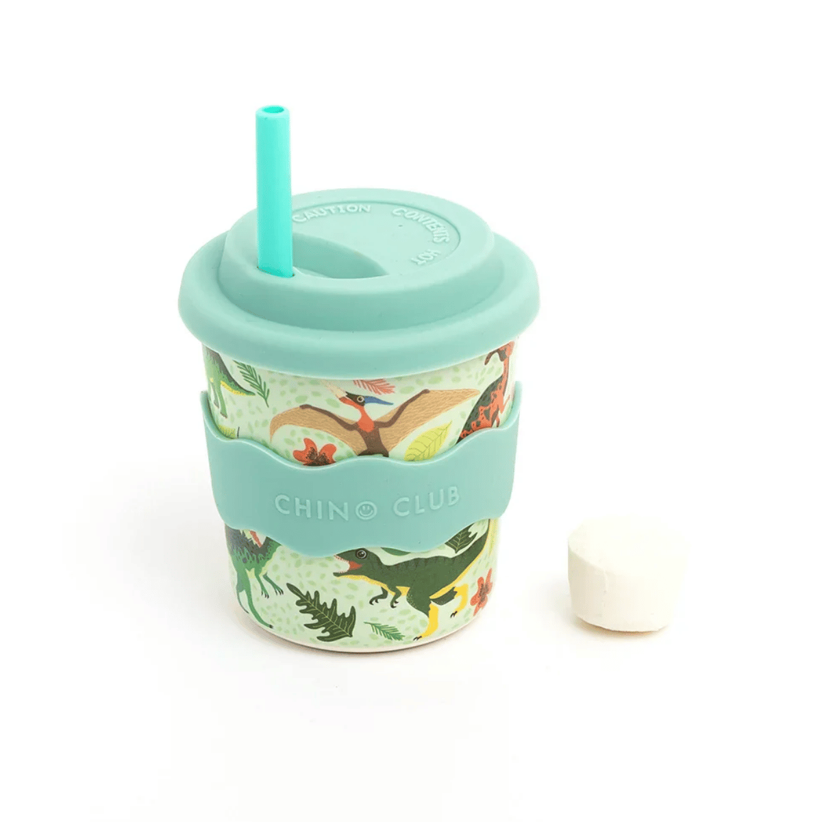 A reusable travel tumbler with a mint green silicone sleeve and lid, featuring a turquoise straw and a colorful dinosaur pattern on the cup body. A white cap is placed to the right of the cup on a clean white background.