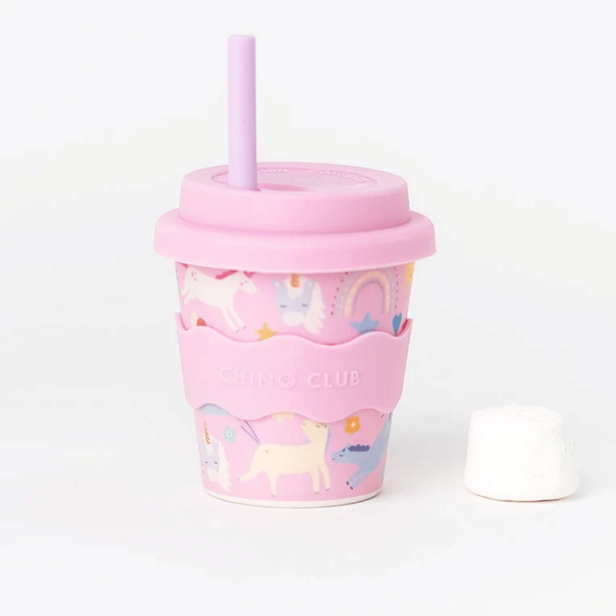A pink silicone travel tumbler cup with a matching straw lid, featuring a pastel unicorn pattern and a pink silicone sleeve with the brand name 'CHINO CLUB'. A small white marshmallow sits to the right on a clean white background.