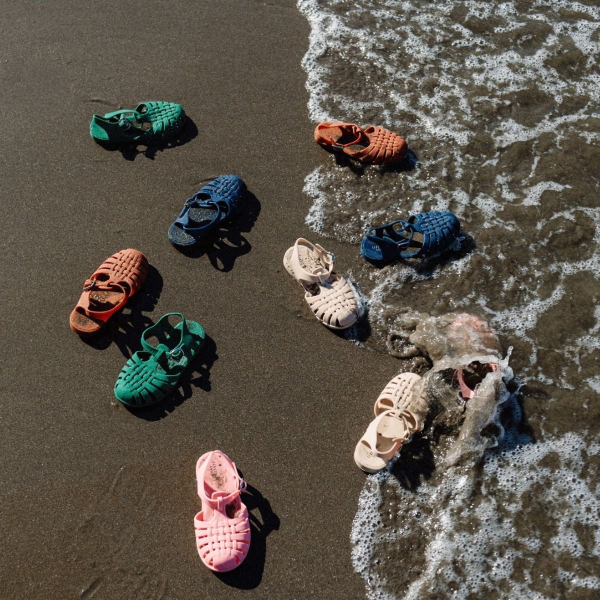 Colorful children's sandals on a sandy beach with waves.