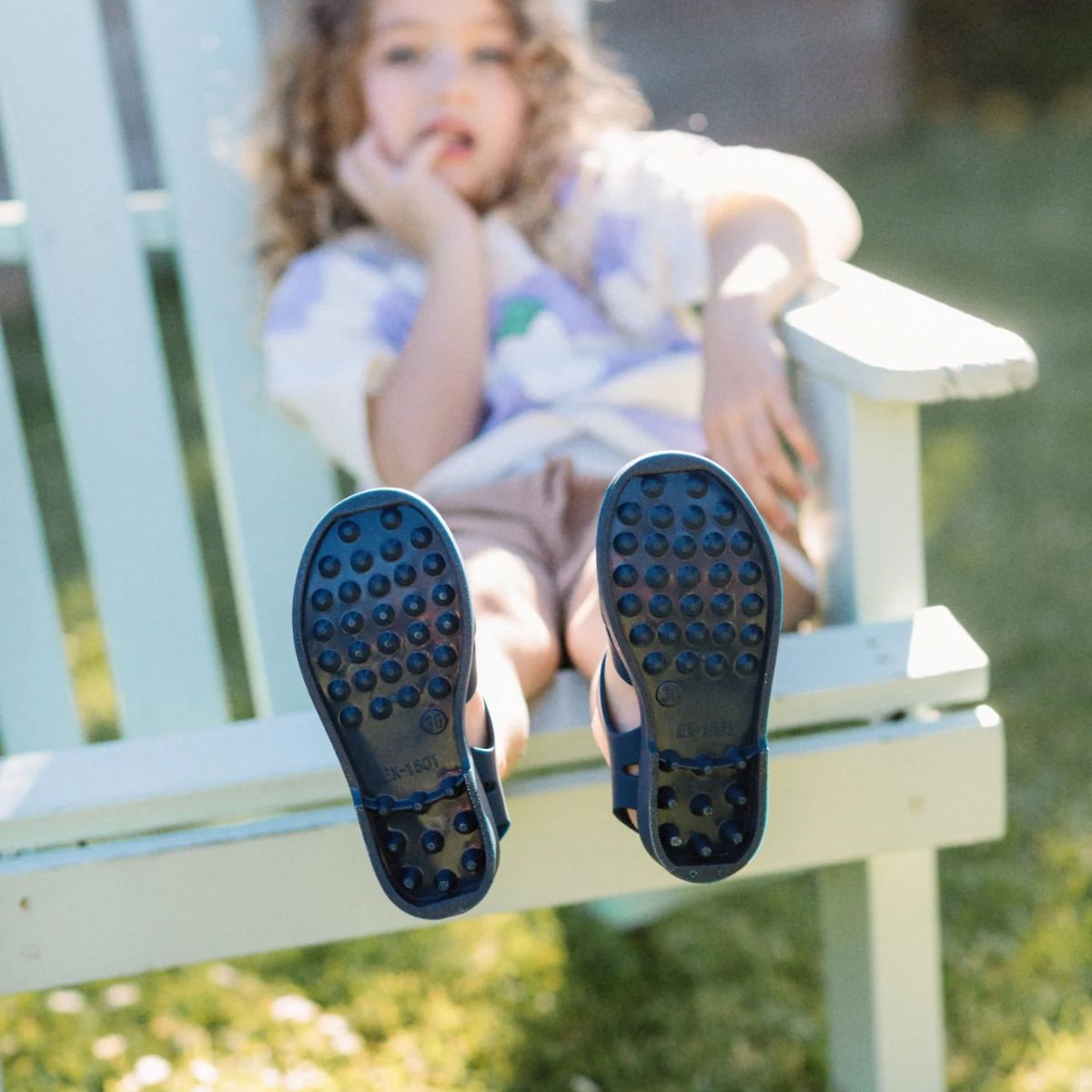 Child sitting on a bench with feet up, wearing blue shoes with textured soles.