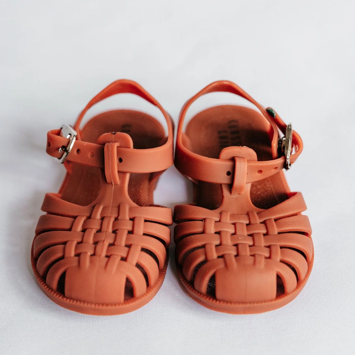 Pair of rust sandals with woven design on a white background