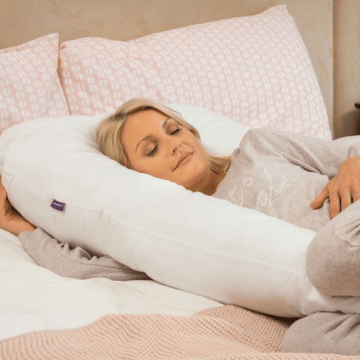 Woman lying in bed with a large white body pillow.