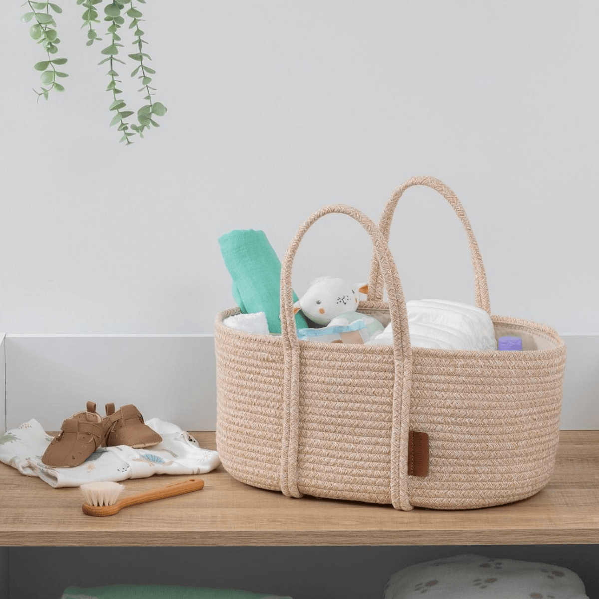 Woven baby basket with baby items on a wooden surface, plant in the corner.