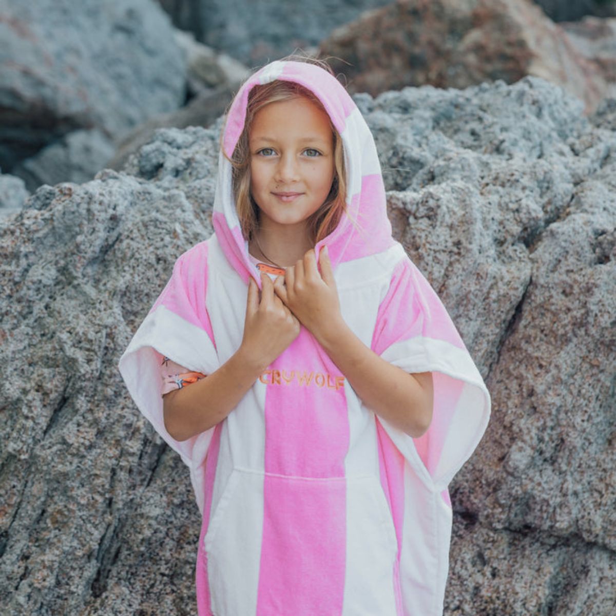 Young girl wearing a pink and white hooded towel on rocky beach
