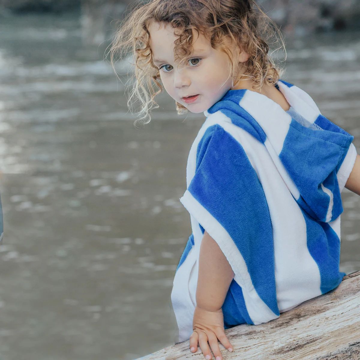 Child wearing a blue and white striped towel by a body of water