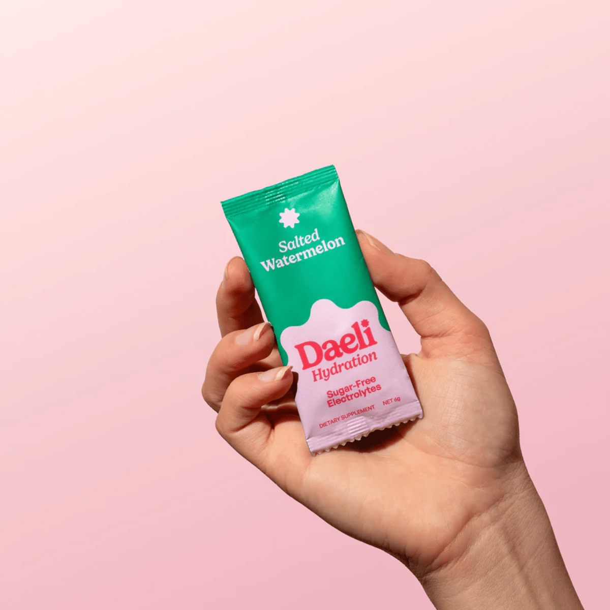 Hand holding a Daeli Hydration packet against a pink background