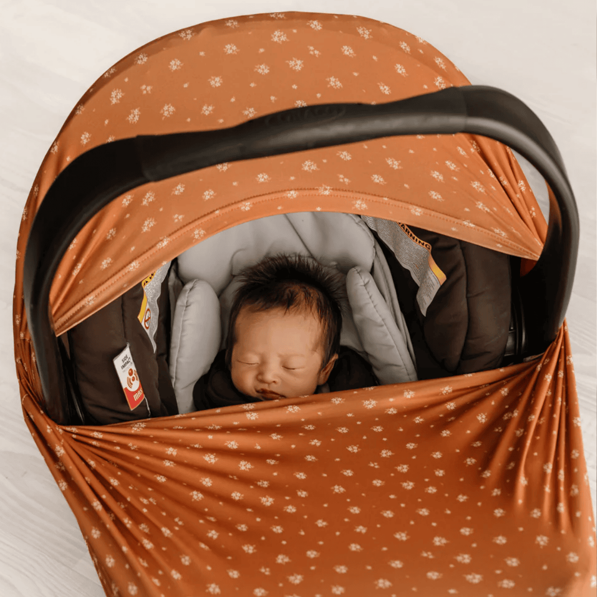 Newborn baby sleeping in a car seat with an orange patterned cover