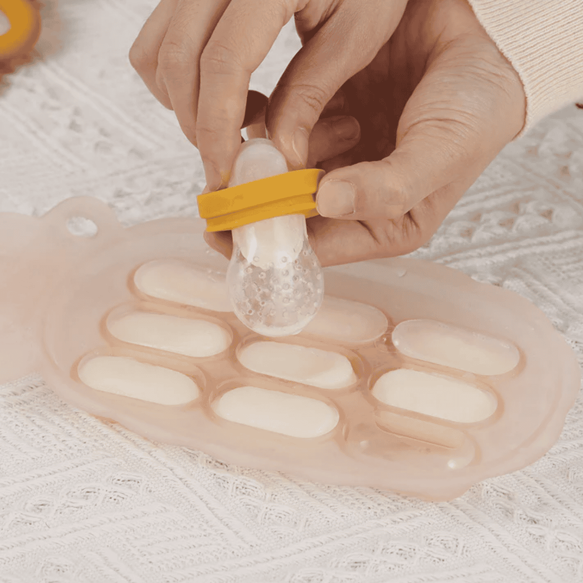 Person using a silicone food cube tray with oval molds on a textured surface.