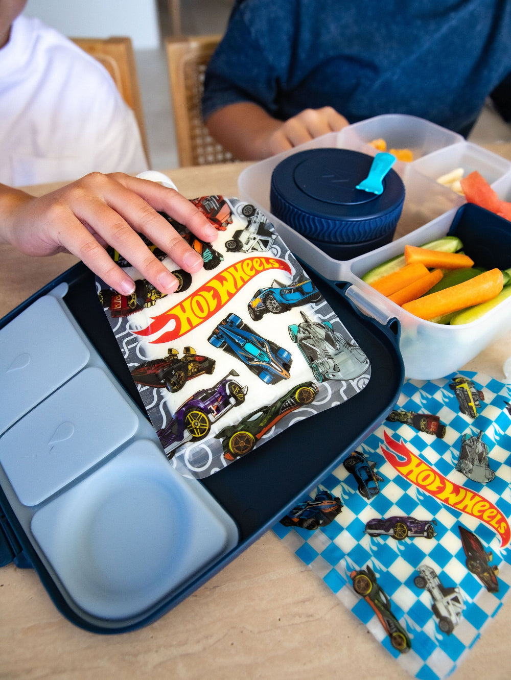 Children playing with Hot Wheels cars in a compartmentalized container on a table.