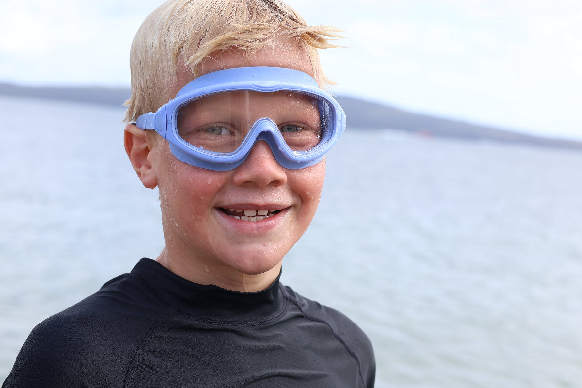 Child wearing blue goggles and a black wetsuit with a blurred water background