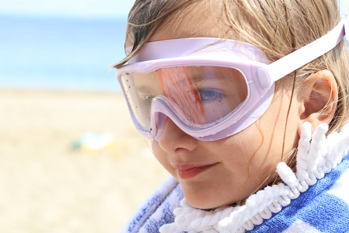 Child wearing goggles and a towel on a beach