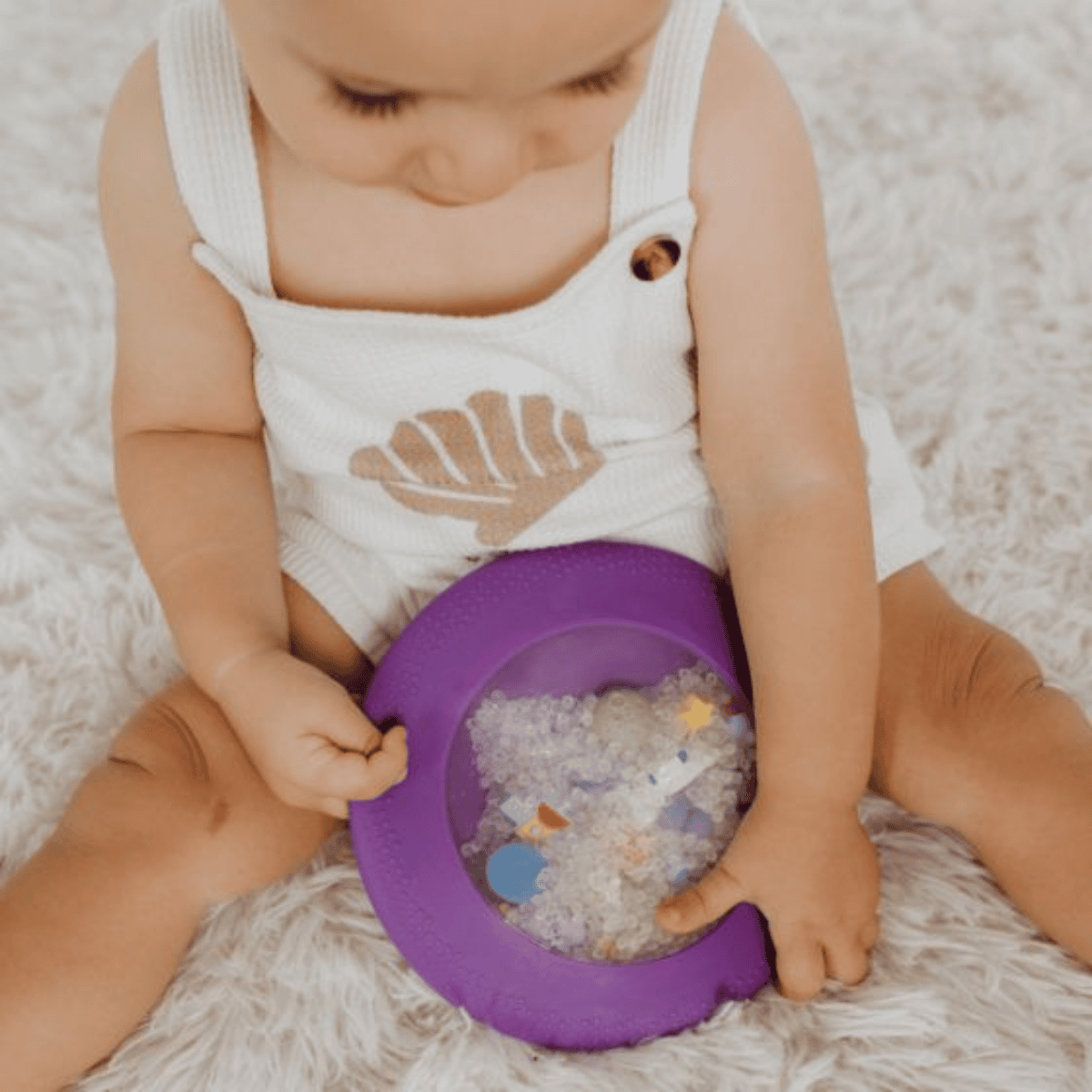 Child playing with a purple bowl filled with small objects on a soft surface