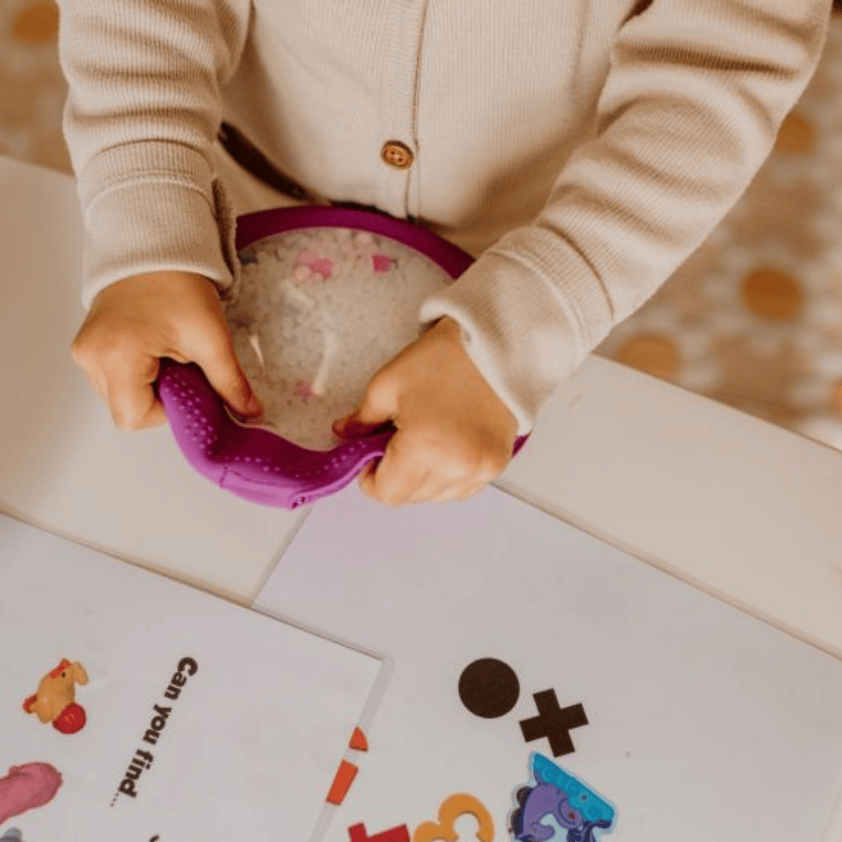 Child playing with a purple toy on a table with educational materials