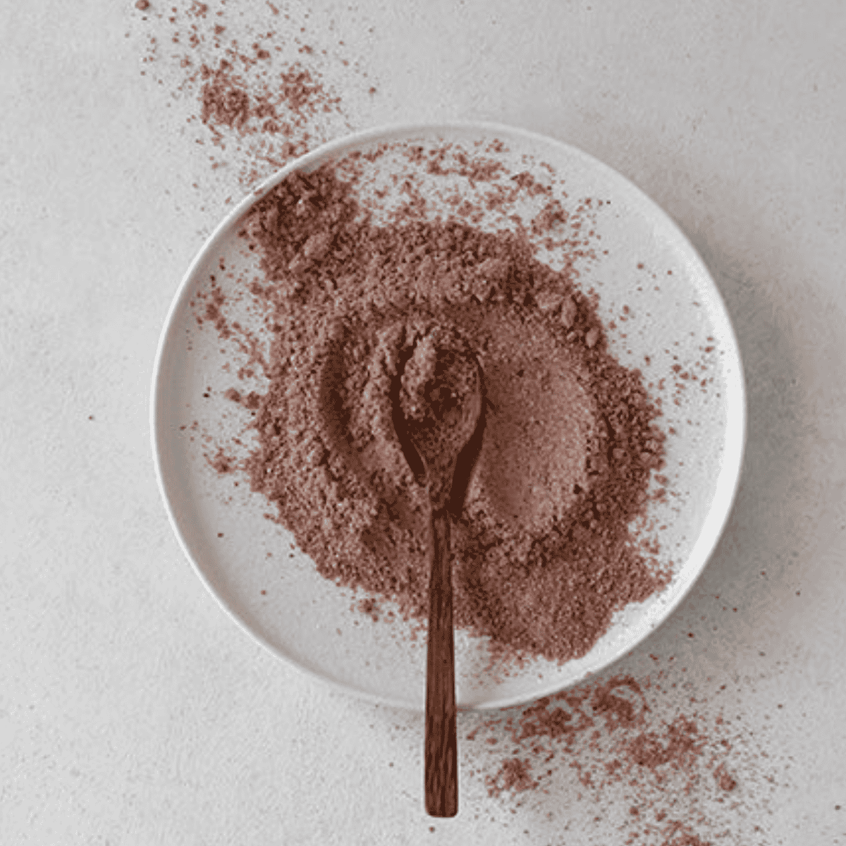 Cocoa powder on a white plate with a wooden spoon