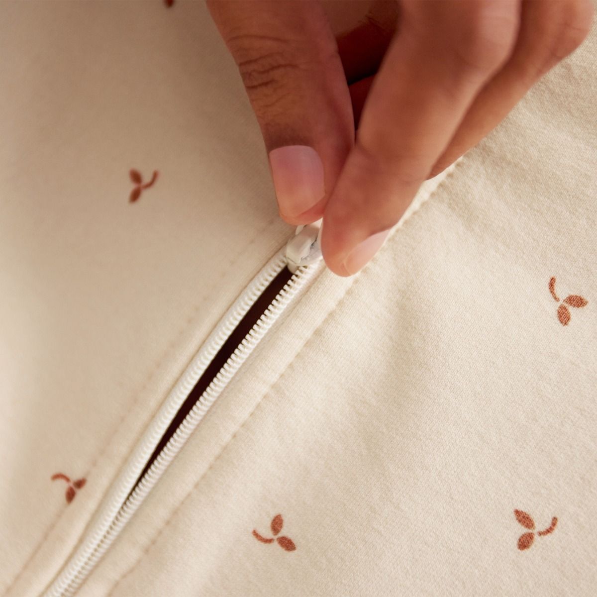 Hand zipping a cream-colored fabric bag with small brown floral patterns.