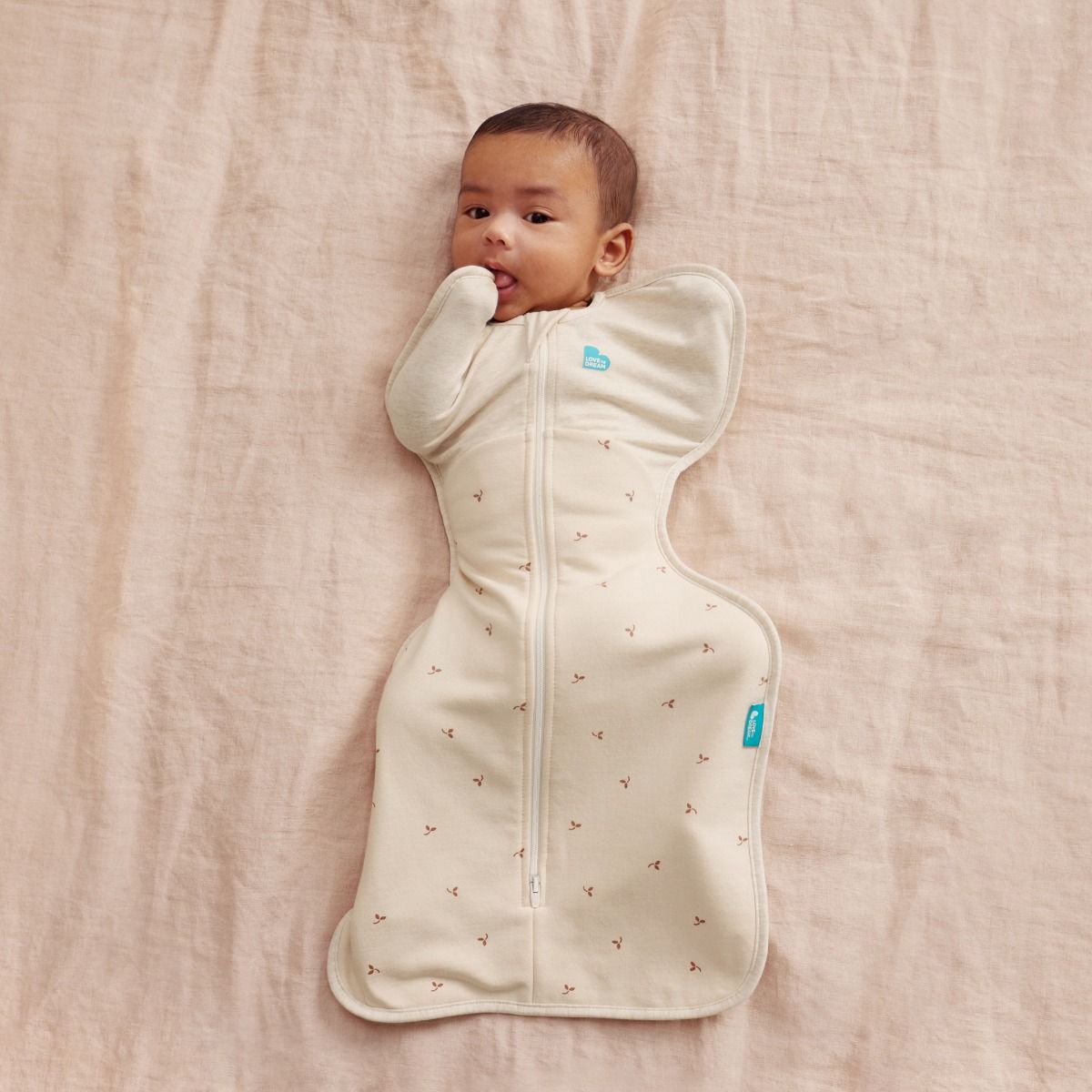 Baby wrapped in a cream-colored swaddle with small patterns on a beige blanket
