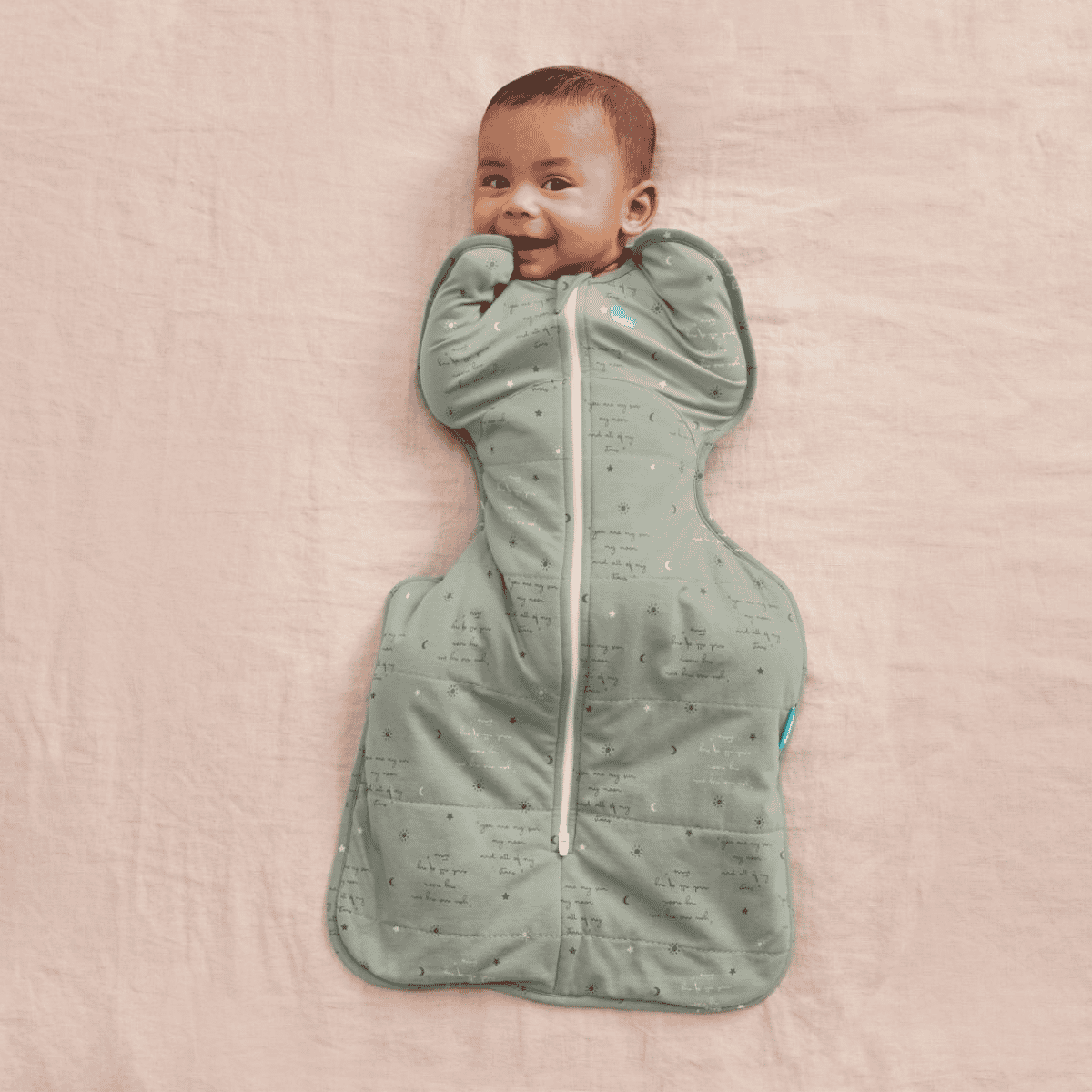 Baby wrapped in a green sleeping bag on a pink blanket
