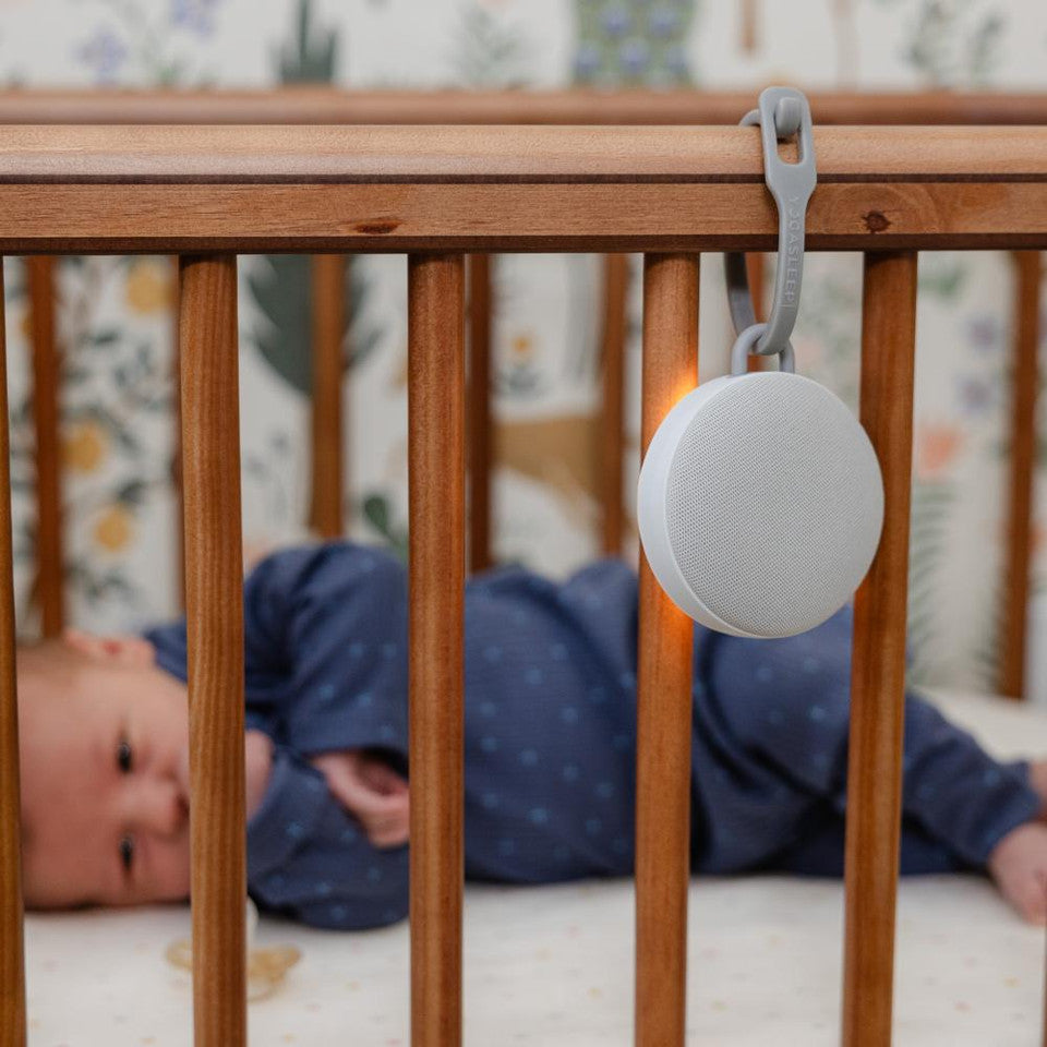 Baby lying in a crib with a white device hanging on the wooden bars.