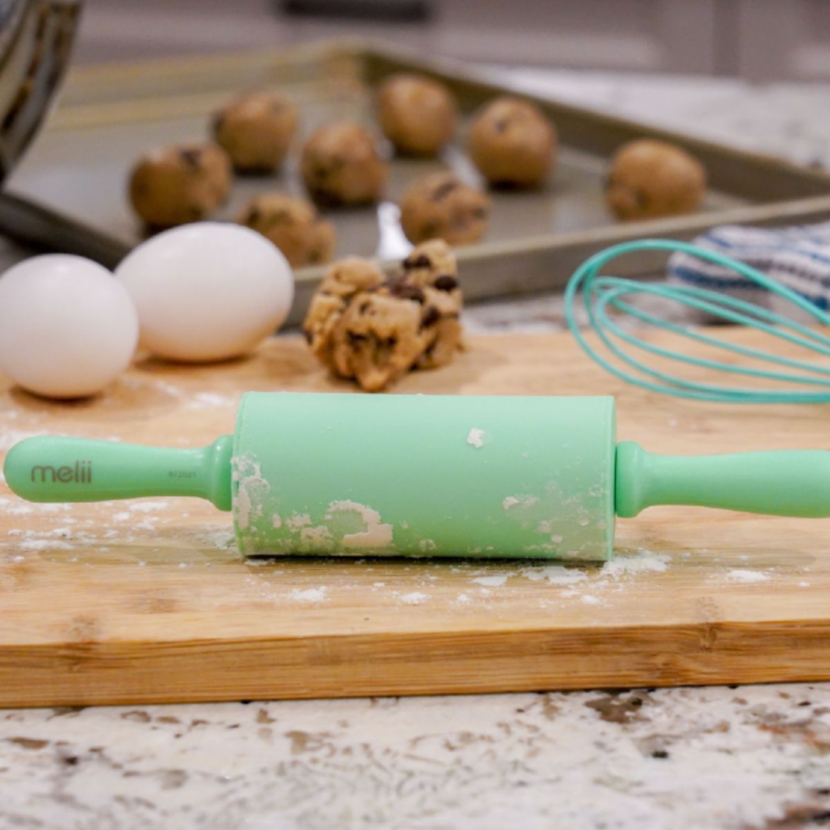 Green rolling pin on a wooden board with cookies and eggs in the background