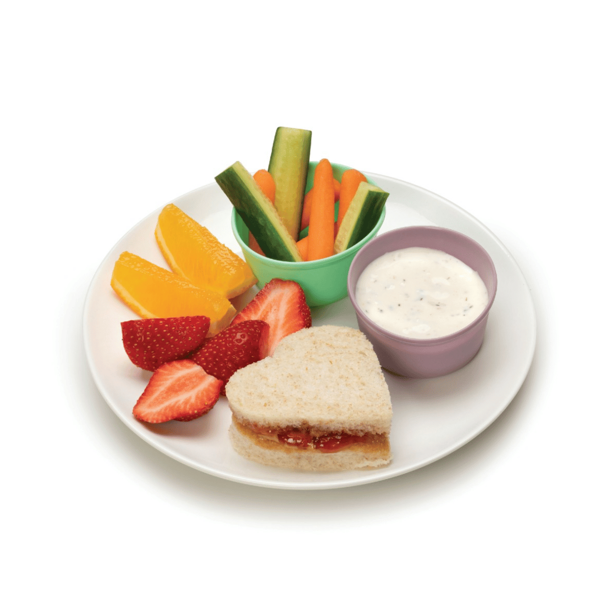 A white plate of healthy snack food featuring a heart-shaped sandwich, sliced strawberries, orange wedges, cucumber and carrot sticks, and a small bowl of white dip on a white background.