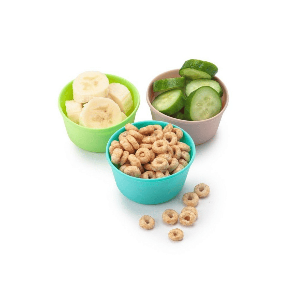 Three small plastic bowls on a white background: a green bowl with banana slices, a beige bowl with cucumber slices, and a turquoise bowl with cereal rings, with a few cereal pieces scattered in front.