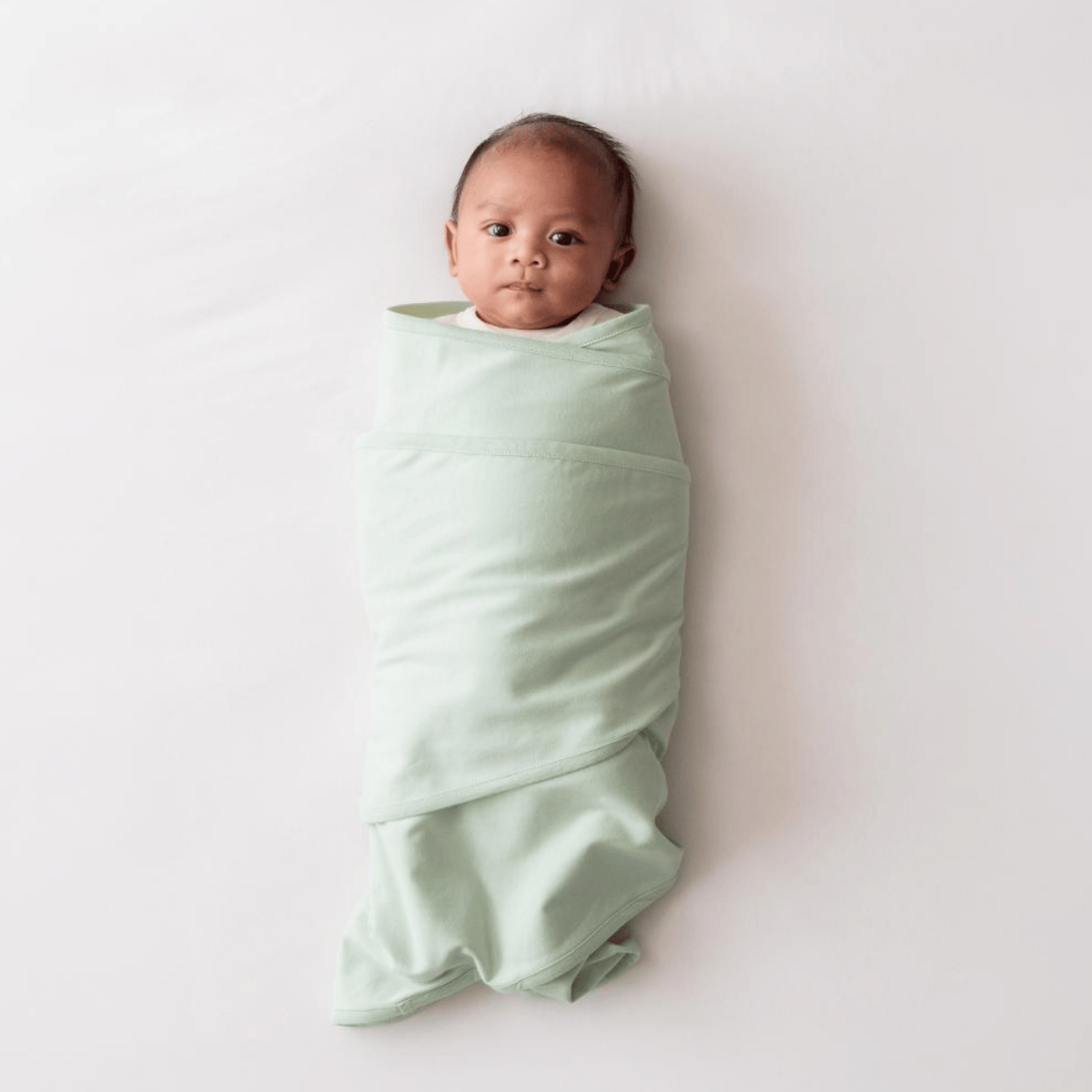 Baby wrapped in a light sage swaddle on a white background