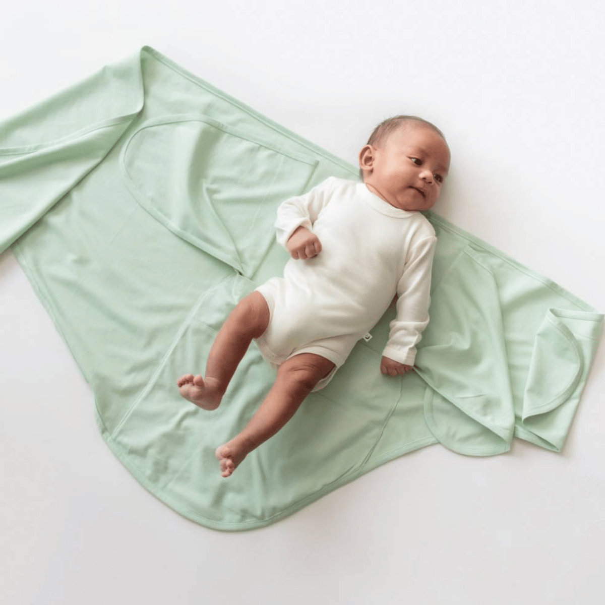 Baby in a white onesie lying on a light green blanket on a white background